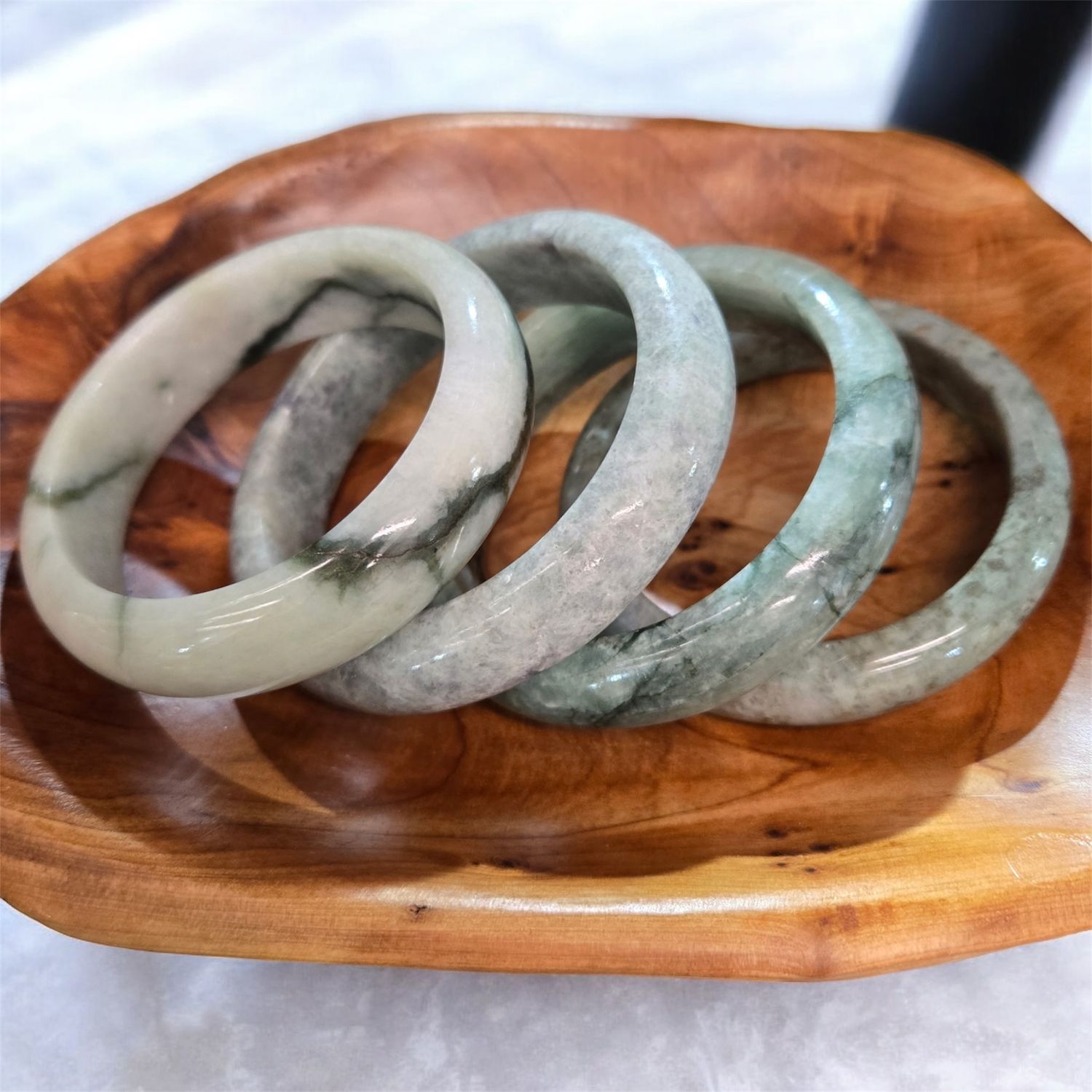 BURMESE JADE BANGLE 14MM 14mm Burmese jade bangle bracelet with natural green and white marbling on a wooden display tray