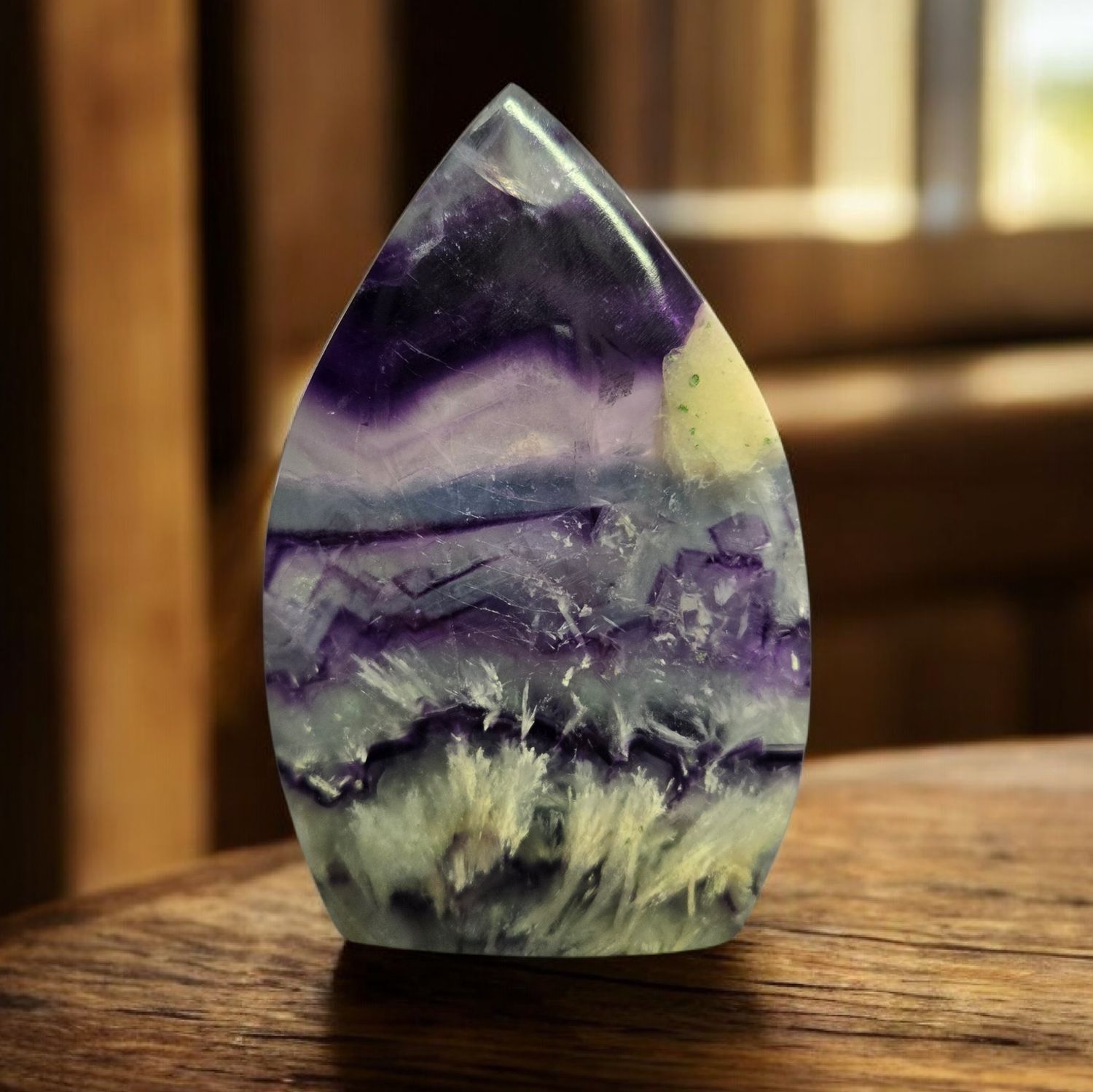 Polished fluorite arrowhead crystal with purple and green banding on wooden surface