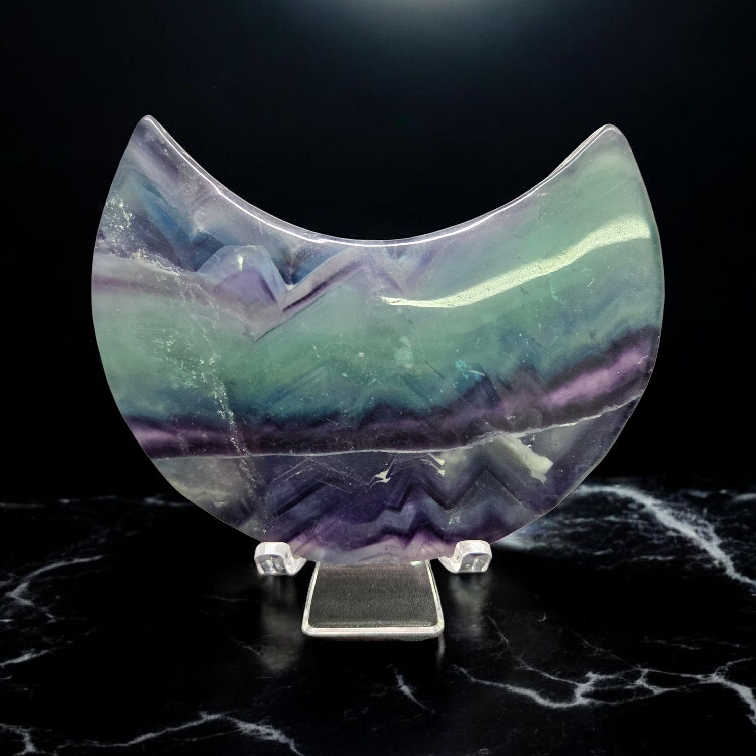 Fluorite moon crystal with green and purple banding displayed on a clear stand
