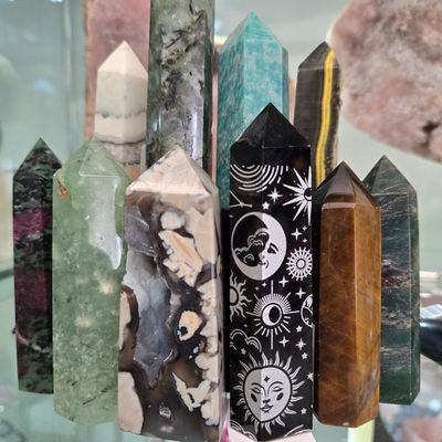 Polished crystal obelisk towers including tiger eye, moss agate, quartz, and engraved black obsidian displayed together.