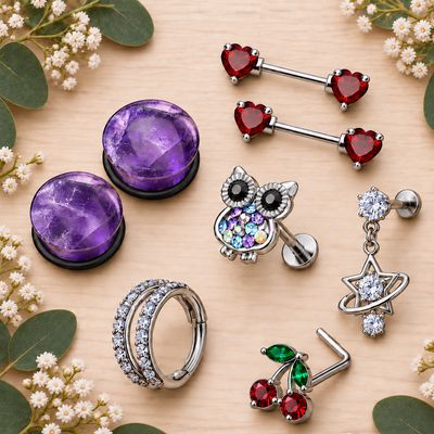 Body jewelry collage on a wooden table with amethyst plugs, heart barbells, owl stud, hoop, celestial stud, and cherries nose