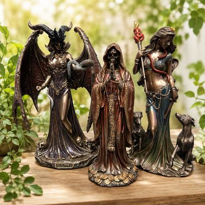 Three detailed deity statues displayed on a light wooden table with greenery in the background at Arkadys Metaphysical Gifts.