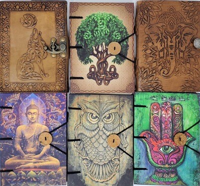 Assorted spiritual journals and spellbooks with embossed leather covers featuring wolf, tree of life, elephant, and a Buddha