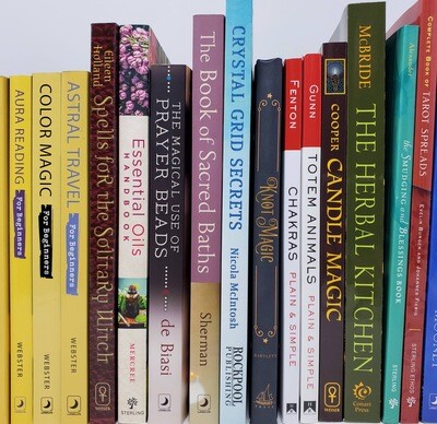 Collection of witchcraft, tarot, chakra, crystal, and herbal magic books displayed upright on a shelf