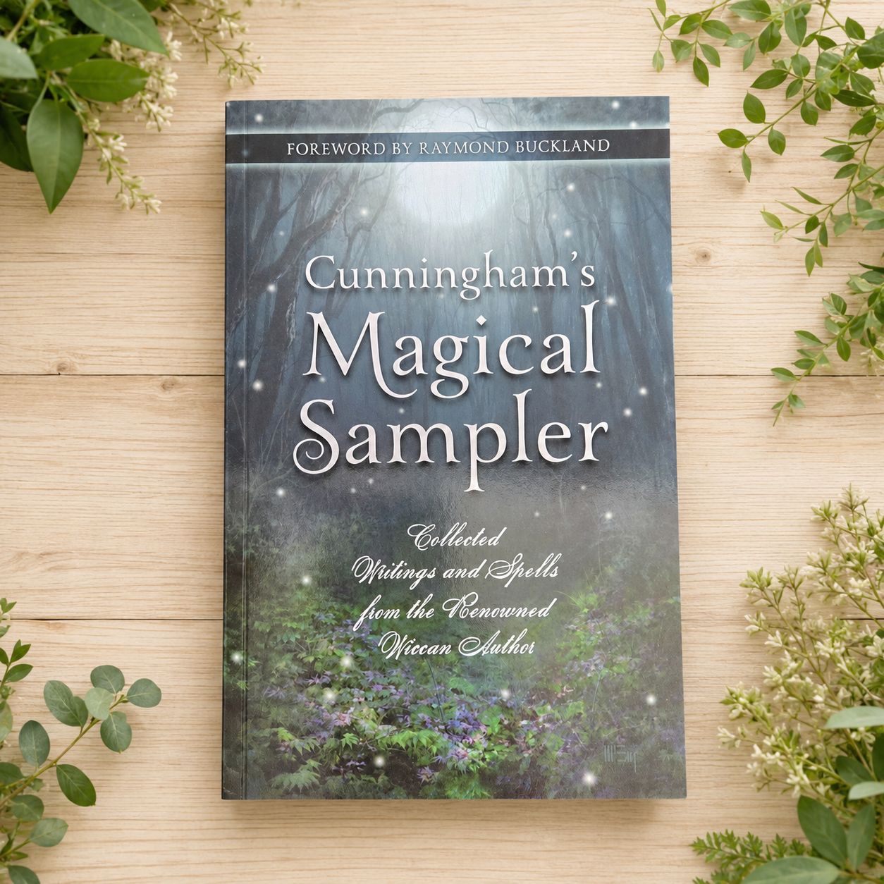 Cunningham’s Magical Sampler by Scott Cunningham on a light wooden table with greenery.