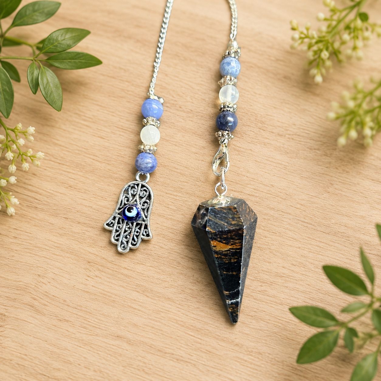 Close-up of Blue tiger eye Hamsa pendulum with blue beads and evil eye charm on a light wooden table