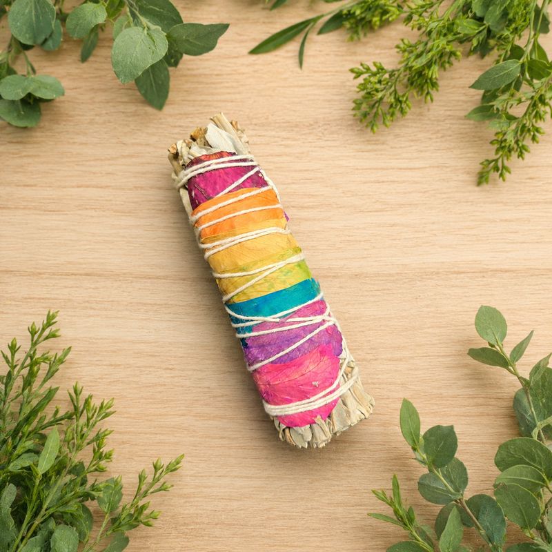 Chakra roses and white sage smudge on a light wooden table with greenery