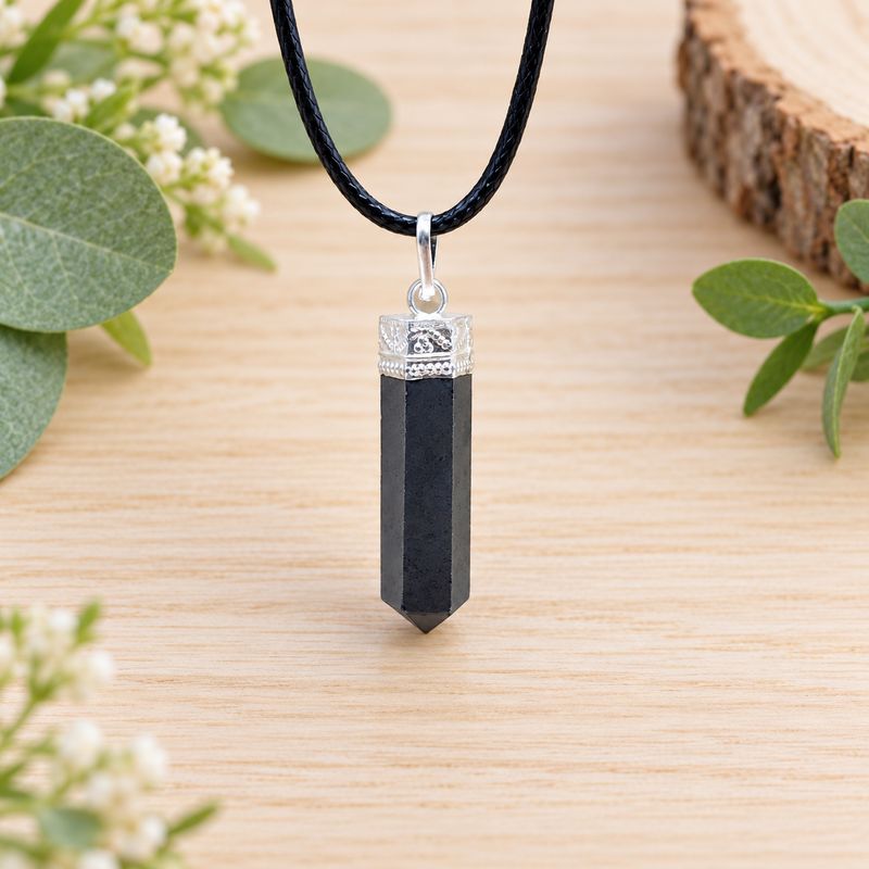 Pyrite pencil pendant necklace with silver-tone cap and black cord displayed on light wood with greenery.