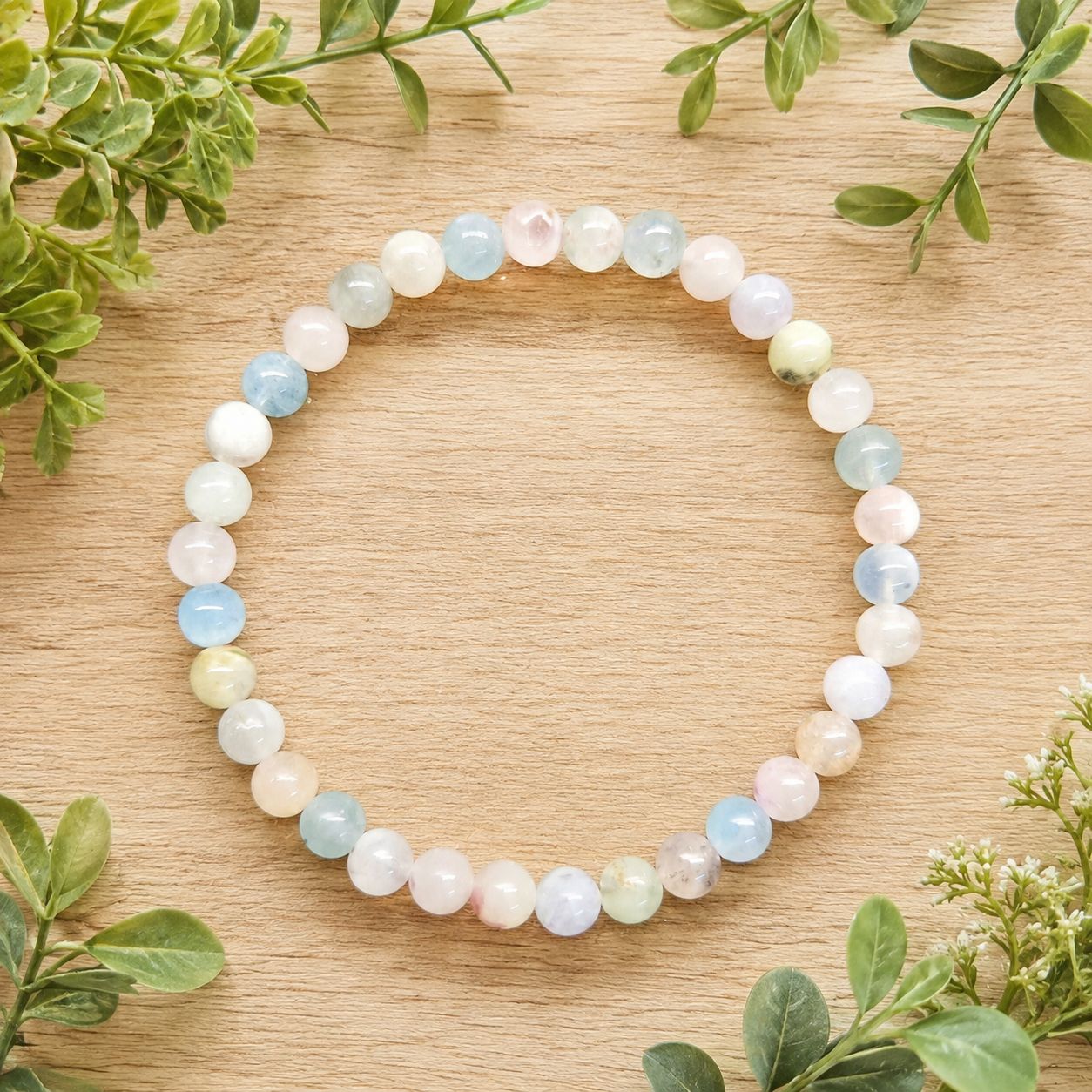 Morganite 6mm gemstone bracelet displayed on a light wooden table with greenery.