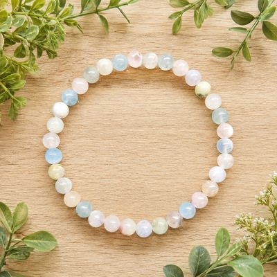 Morganite 6mm gemstone bracelet displayed on a light wooden table with greenery.