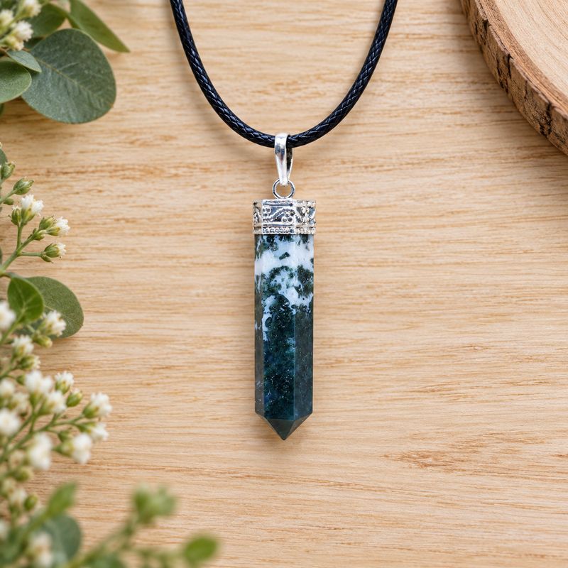 Moss agate pencil pendant necklace with silver tone cap on black cord displayed on light wood with greenery