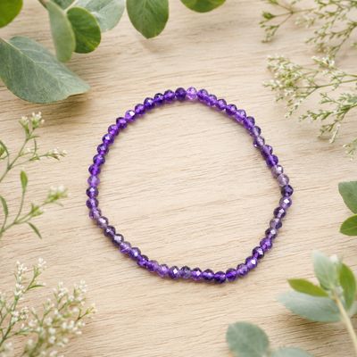 Faceted Amethyst 4mm gemstone bracelet displayed on a light wooden table with greenery.