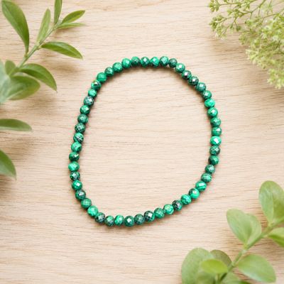 Faceted Malachite 4mm gemstone bracelet displayed on a light wooden table with greenery.