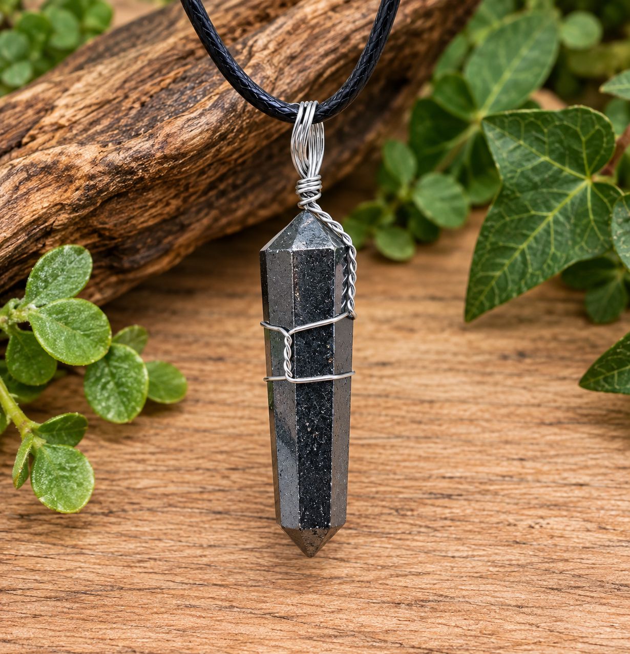 Hematite point wire wrap necklace with silver-tone wire and black cord displayed on natural wood with greenery.