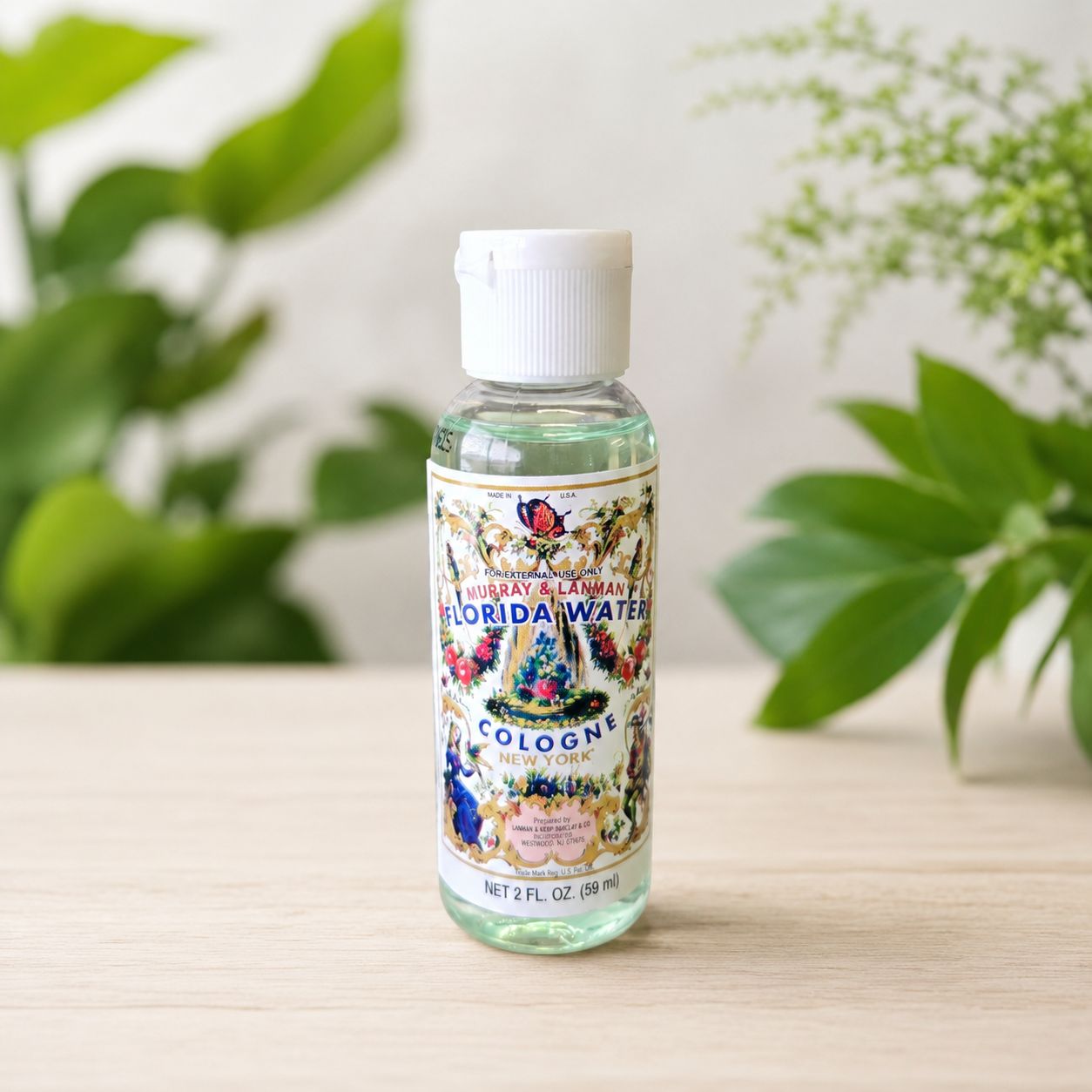 Travel size 2 oz Florida Water Cologne bottle on a light wooden table with greenery.