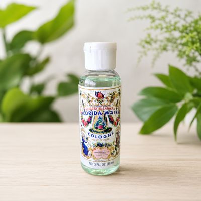 Travel size 2 oz Florida Water Cologne bottle on a light wooden table with greenery.