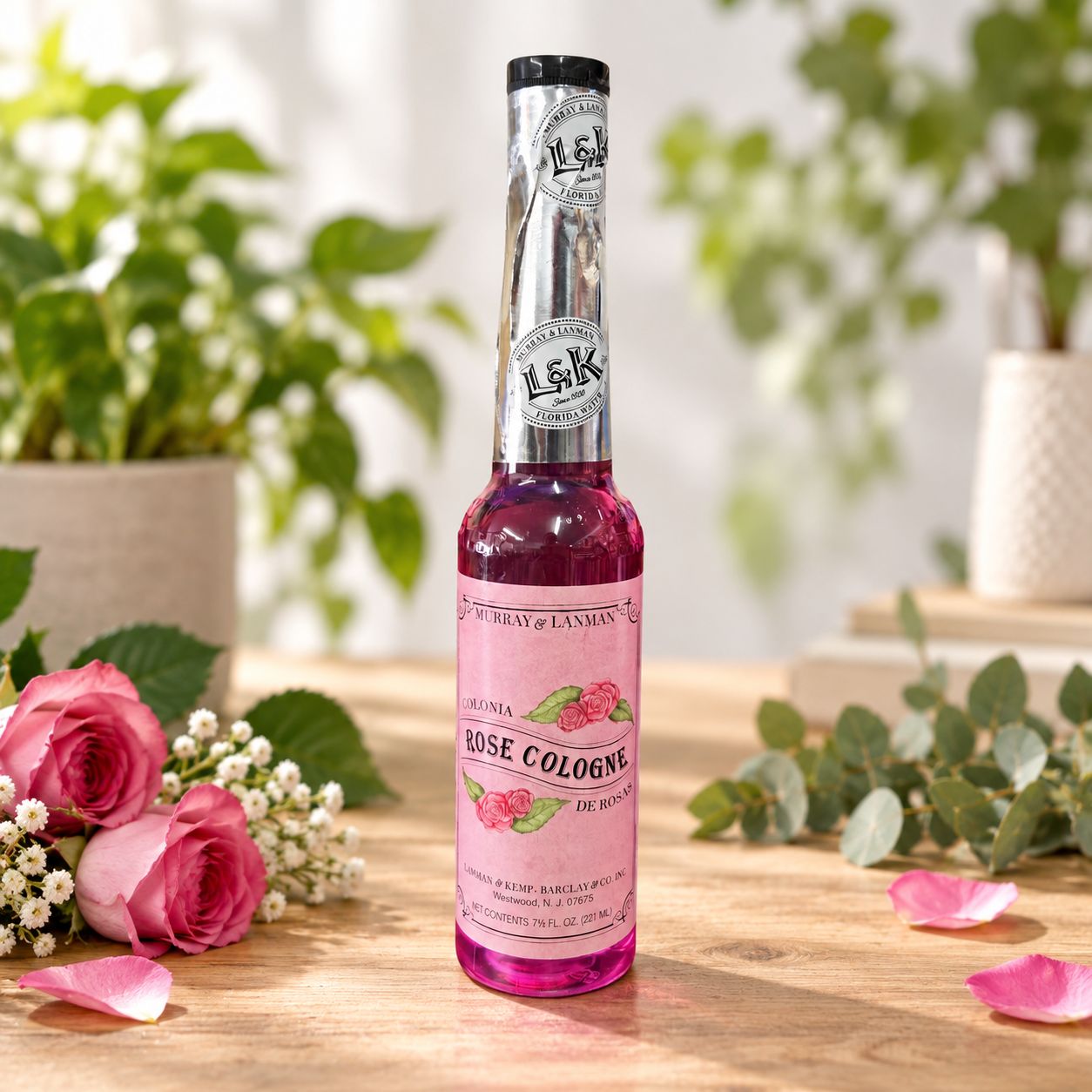 Rose Cologne bottle on a light wooden table with greenery and pink roses.