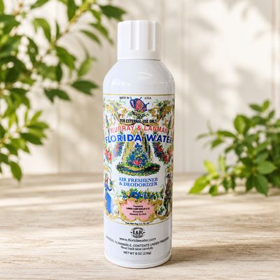 Florida Water Aerosol Spray 8 oz bottle on a light wooden table with greenery.