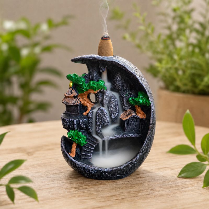 Village waterfall backflow incense burner with cascading smoke on a light wooden table with greenery.