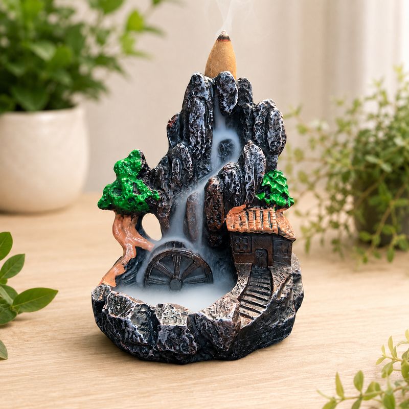 Watermill waterfall backflow incense burner with cascading smoke on a light wooden table with greenery.