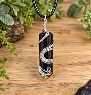 Ornate wire wrap black tourmaline necklace on black cord over light wood with greenery.