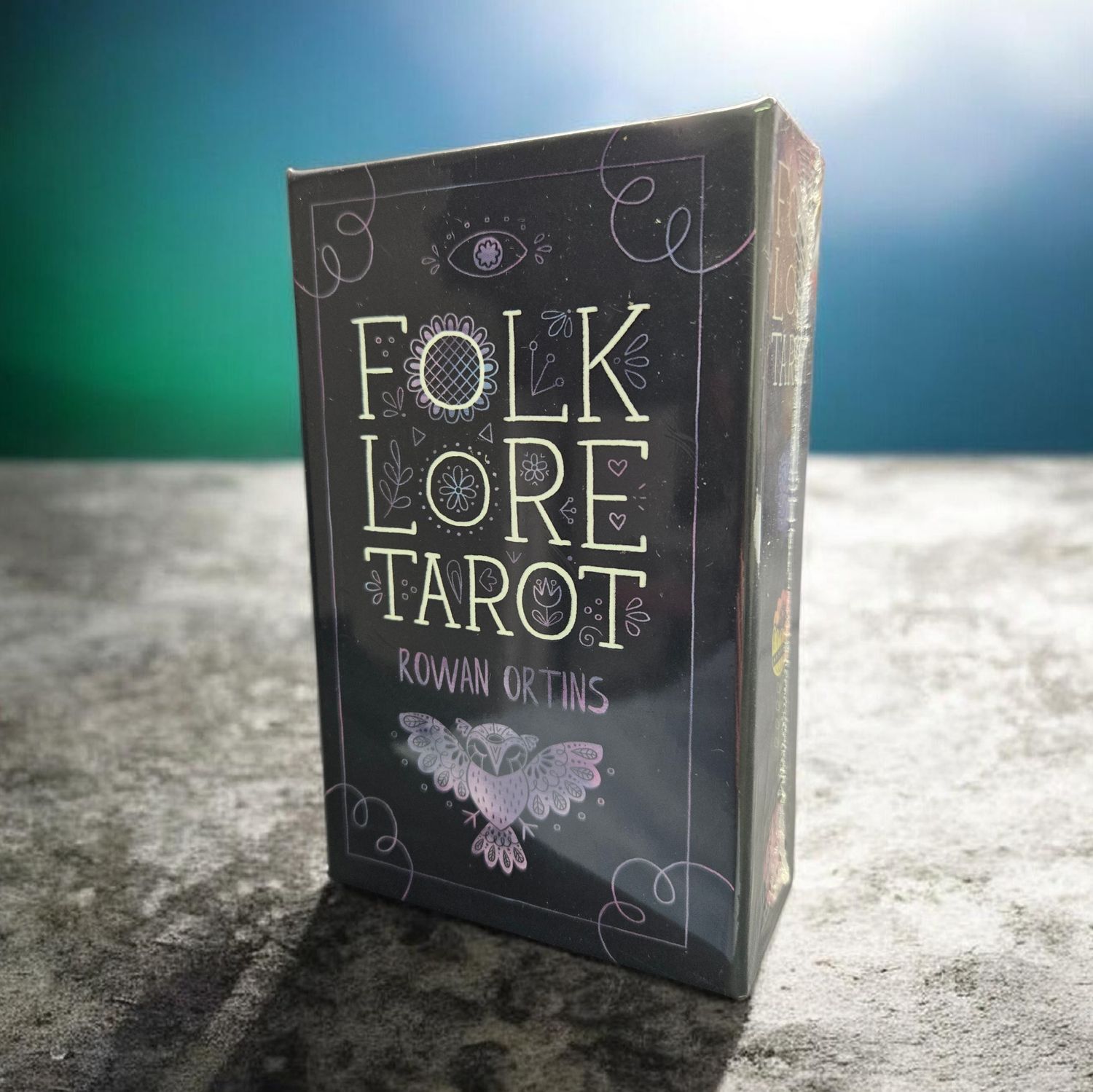 Folklore Tarot deck by Rowan Ortins with black gilt-edged cards and illustrated guidebook.