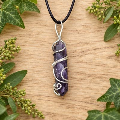 Ornate wire wrap amethyst point necklace on black cord over light wood with greenery.