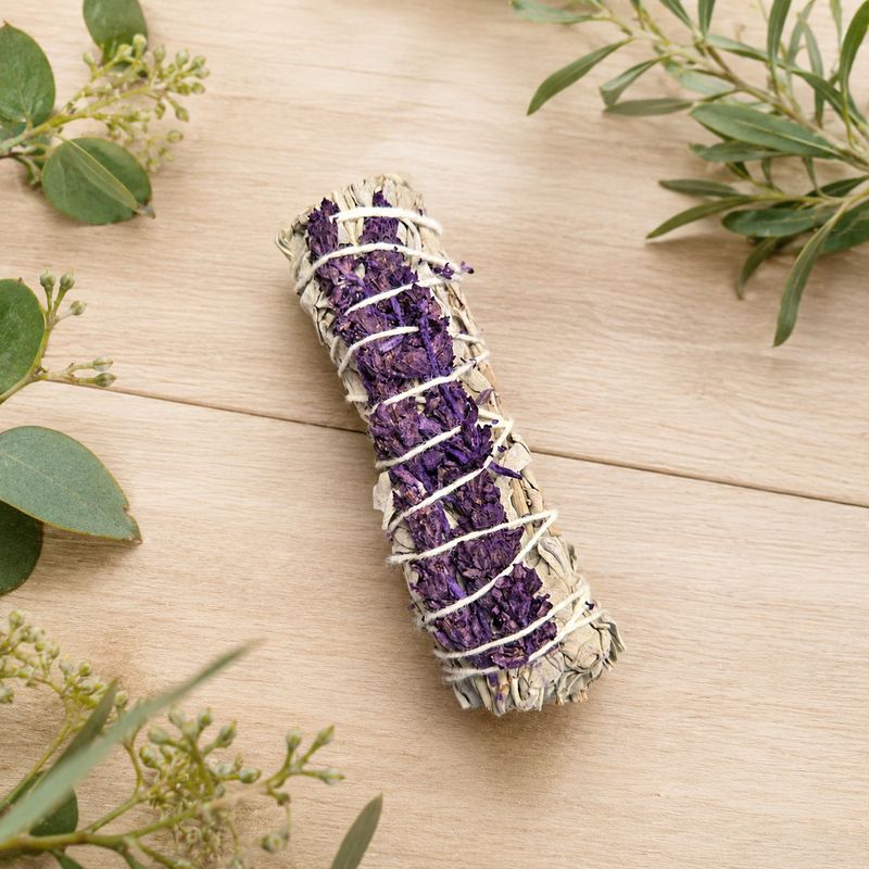 White sage and royal lavender smudge on a light wooden table with greenery