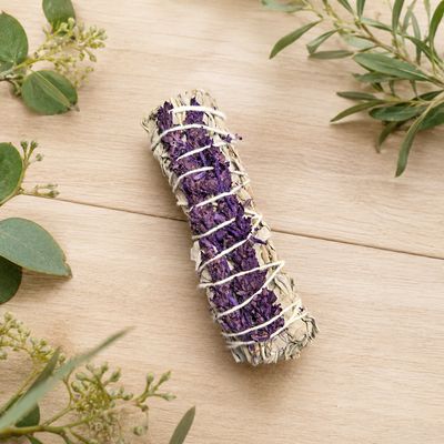 White sage and royal lavender smudge on a light wooden table with greenery
