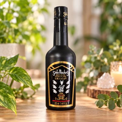 Siete Machos Cologne 7.44 oz black bottle displayed on a light wooden table with greenery.