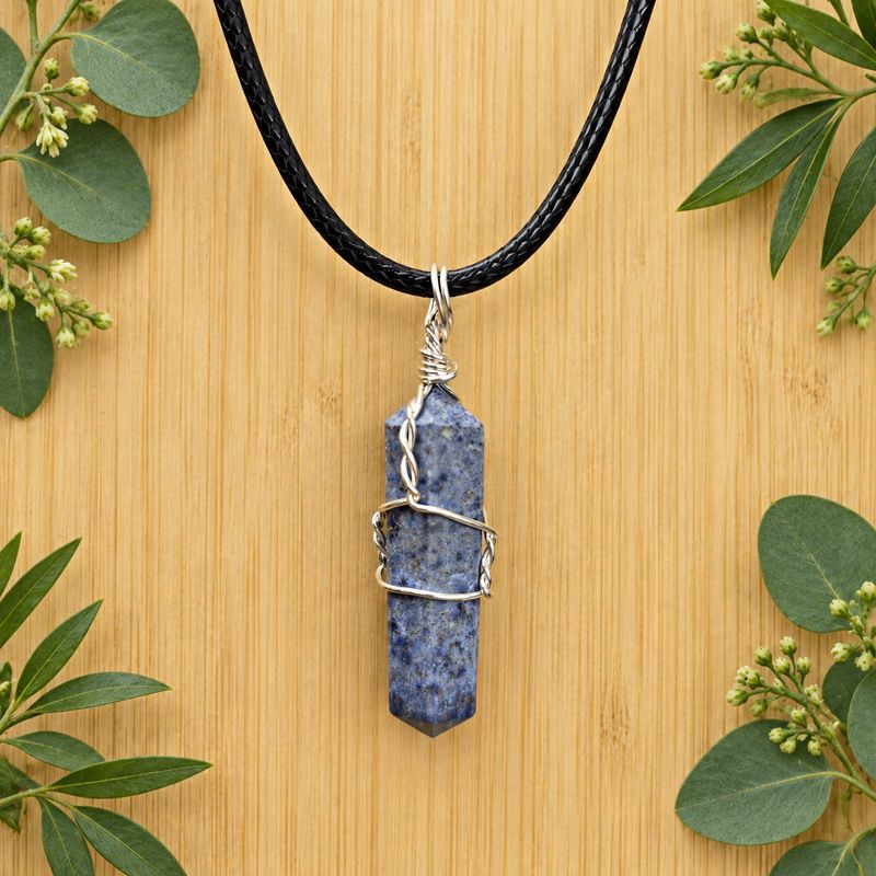 Dumortierite wire wrap pendant necklace on black cord over light wood with greenery.