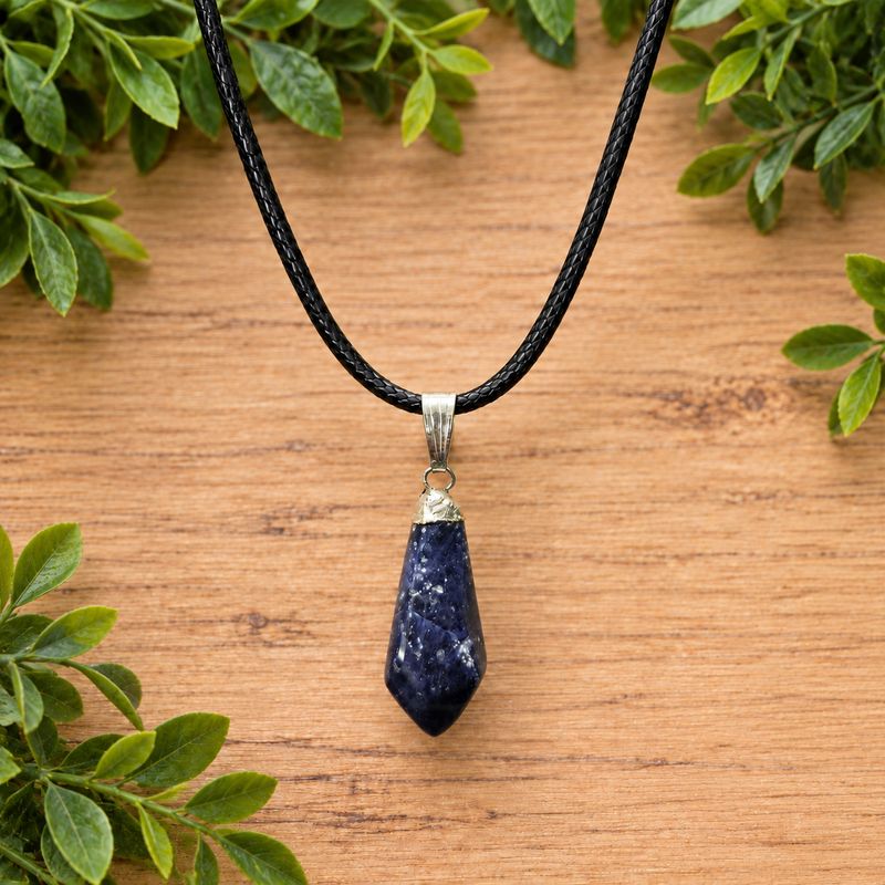 Sodalite faceted point pendant necklace on a black braided cord over light wood with green leaves.