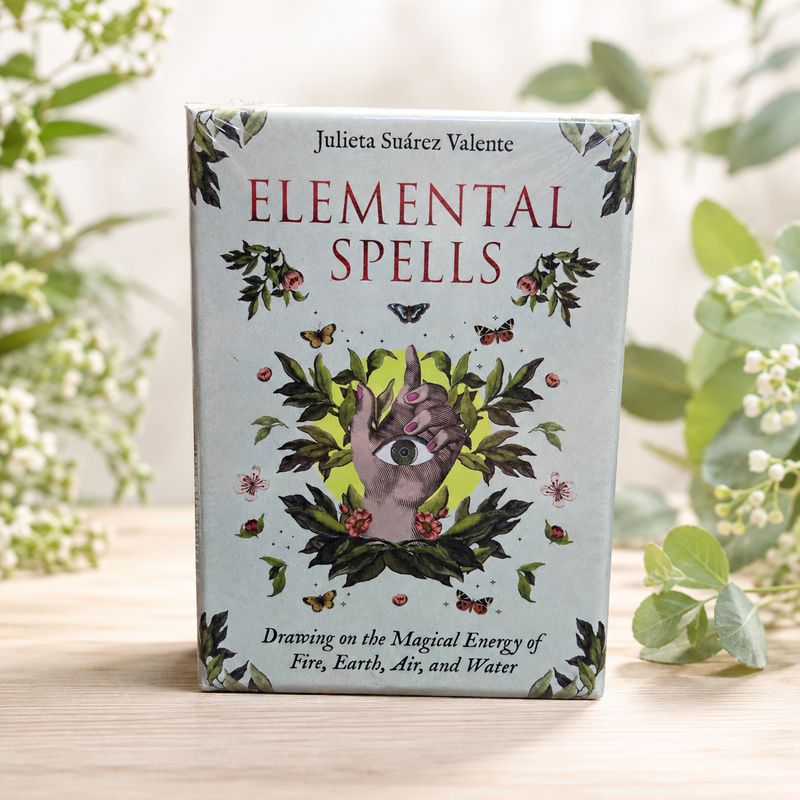 Elemental Spells Oracle Deck with botanical hand and eye artwork displayed on a light wooden table.