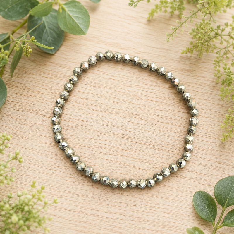 Faceted Pyrite 4mm gemstone bracelet displayed on a light wooden table with greenery.