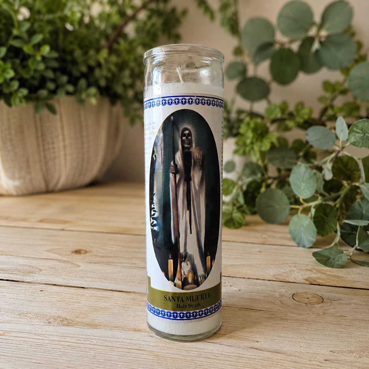 White Santa Muerte prayer jar candle on light wooden altar table with greenery background at Arkadys Metaphysical Gifts.