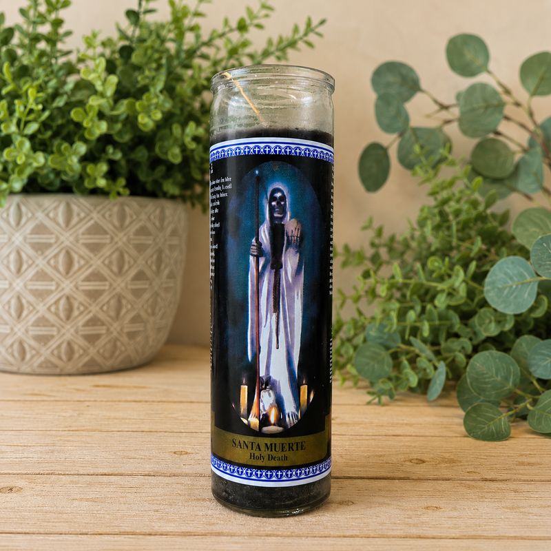 Black Santa Muerte prayer jar candle on light wooden altar table with greenery background at Arkadys Metaphysical Gifts.
