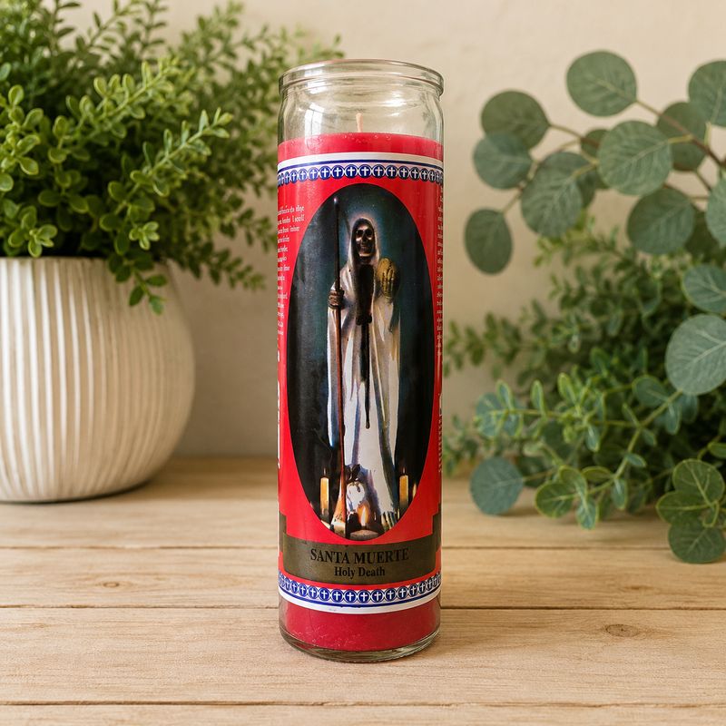 Red Santa Muerte prayer jar candle on light wooden altar table with greenery background at Arkadys Metaphysical Gifts.