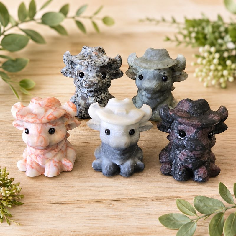 Highland Cow Carvings made from assorted crystals on a light wooden table with greenery.