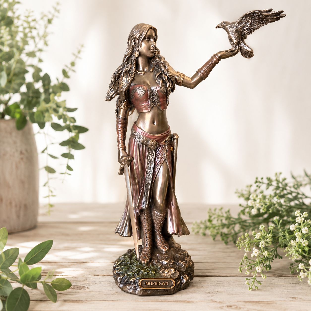 Hand painted Morrigan Celtic goddess statue with raven, sword, bronzed finish, and rocky base on a light wooden table