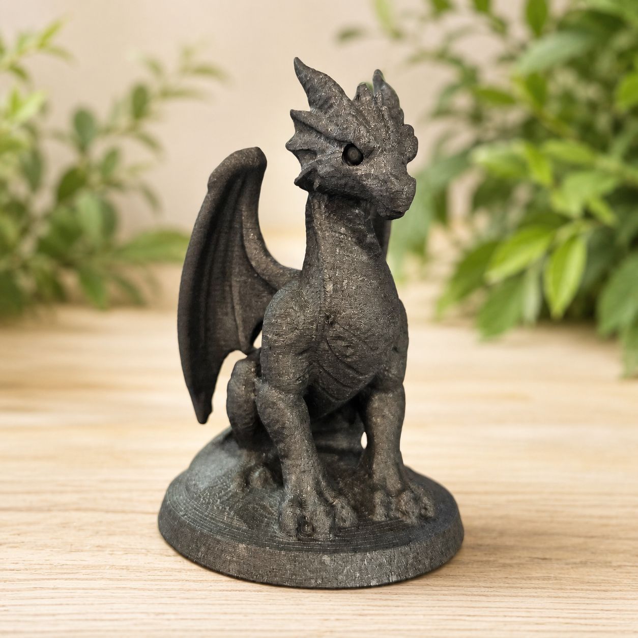 Shungite dragon carving on light wooden table with greenery background.