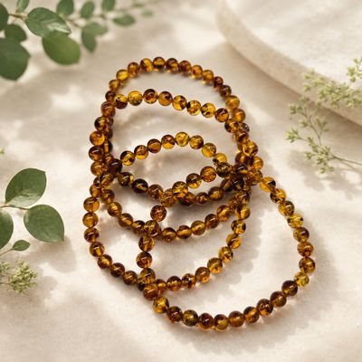 Natural Amber 6mm stretch bracelet with golden amber beads and greenery background.