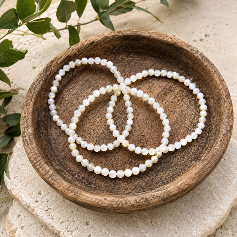 4mm Mother of Pearl faceted bracelets in rustic wooden bowl on stone altar with greenery.