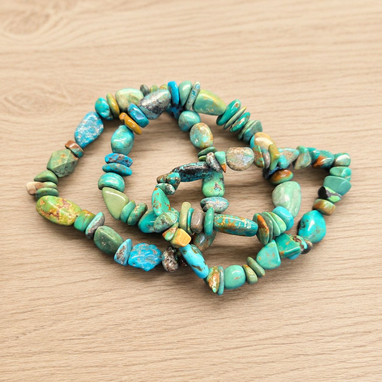 Multiple pebbles turquoise stretch bracelets with polished blue-green stone beads on a wooden table.