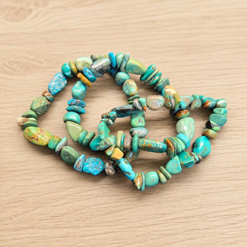 Multiple pebbles turquoise stretch bracelets with polished blue-green stone beads on a wooden table.