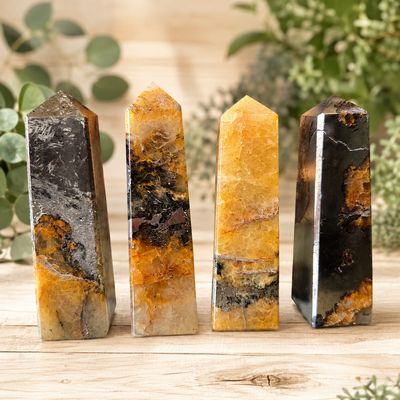 Golden Healer and Pyrite crystal obelisks on a light wooden table with greenery at Arkady's Metaphysical Gifts.