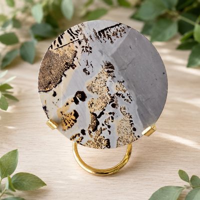 Picture jasper disc slab with gold stand displayed on a light wooden table with greenery.