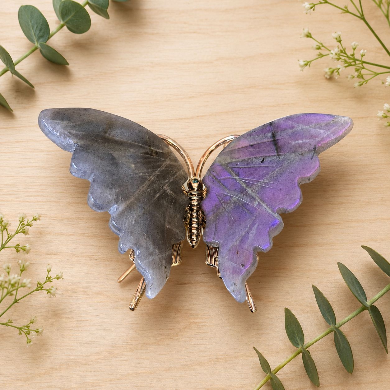 Labradorite butterfly carving on light wooden table with greenery