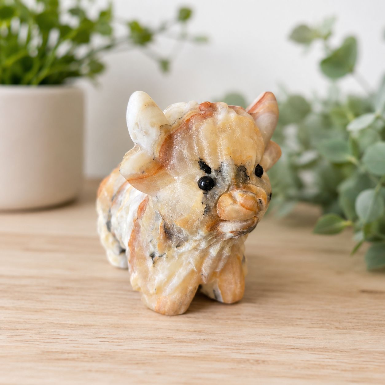 Large banded orange calcite highland cow carving on wooden table with greenery.