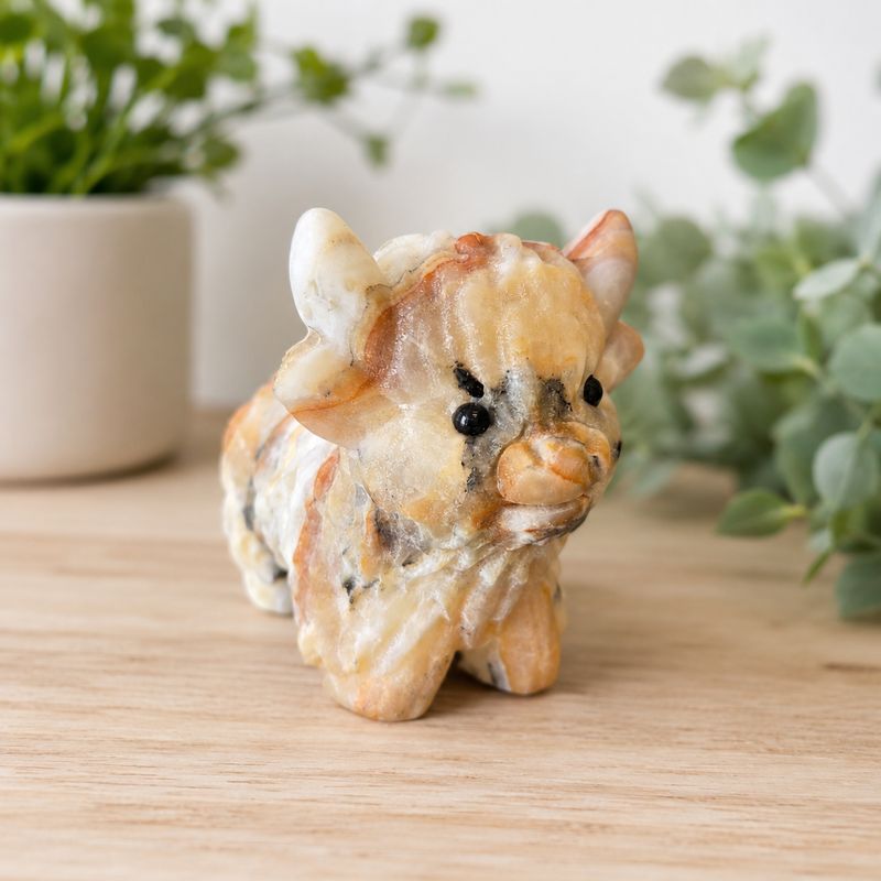 Large banded orange calcite highland cow carving on wooden table with greenery.
