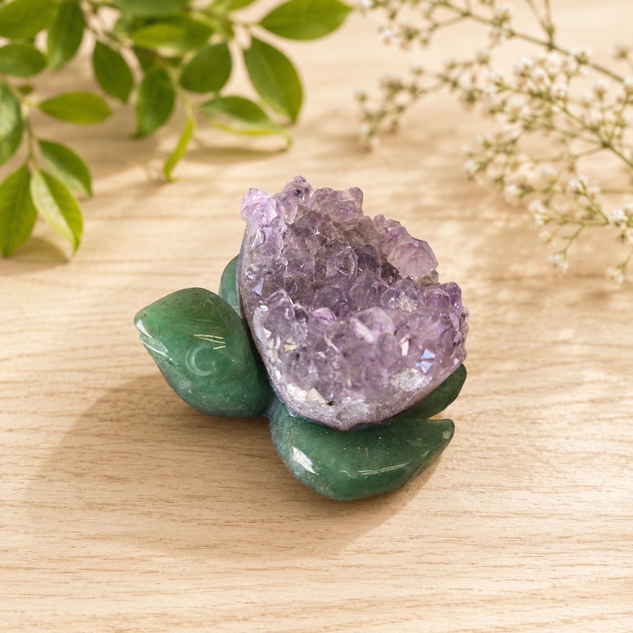 Druzy Amethyst and Green Aventurine sea turtle carving on a light wooden table with greenery.
